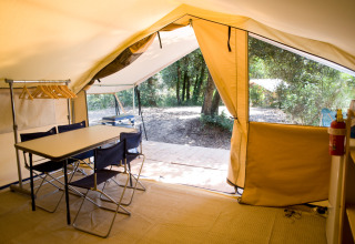 Binnenaanzicht van een safaritent met tafel, stoelen en kledinghangers, bij Huttopia Oléron les Pins in Frankrijk.
