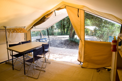 Innenansicht eines Safari-Zelts mit Tisch, Stühlen, Kleiderbügeln und Blick ins Grüne bei Huttopia Oléron les Pins.
