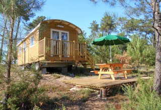 Una casetta in legno chiamata Roulotte con veranda e tavolo da picnic nei boschi di Huttopia Landes Sud, Francia.