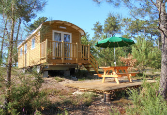 Una casetta in legno chiamata Roulotte con veranda e tavolo da picnic nei boschi di Huttopia Landes Sud, Francia.
