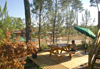 Un niño se sienta en una mesa de picnic de madera junto a una cabaña en el bosque en Huttopia Landes Sud, Francia.