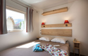 Acogedor dormitorio de cabaña con cama doble, vista exterior a la naturaleza y decoración de madera clara.