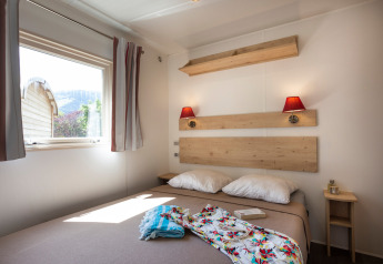 Acogedor dormitorio de cabaña con cama doble, vista exterior a la naturaleza y decoración de madera clara.