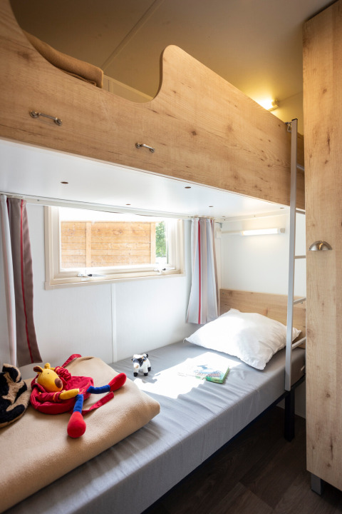 Lichte kamer met stapelbed in een hut, speelgoed op het onderste bed en een raam met gordijnen.