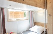 Ein helles Etagenbettzimmer in einer Hütte mit Spielsachen auf dem Bett und einem Fenster mit Vorhängen.