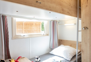 Habitación luminosa con litera en una cabaña, juguetes sobre la cama inferior y ventana con cortinas.