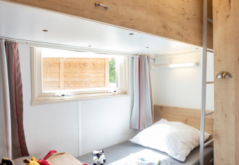 Habitación luminosa con litera en una cabaña, juguetes sobre la cama inferior y ventana con cortinas.