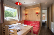 Acogedora cabaña con mesa de comedor, sofá rojo floral, ventana con vista natural y toques de madera.