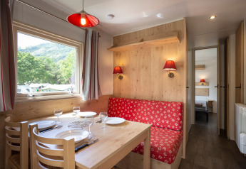 Acogedora cabaña con mesa de comedor, sofá rojo floral, ventana con vista natural y toques de madera.