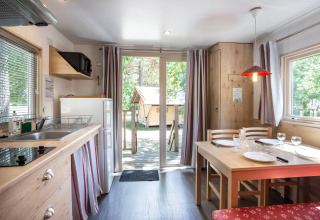 Knus hutinterieur met keuken, eettafel en zicht op terras en groene natuur buiten het raam.