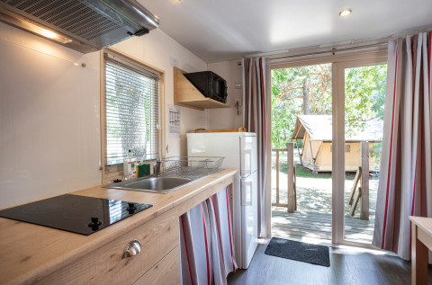 Cucina accogliente in cabina con porte a vetri e vista su veranda e tenda tra gli alberi all’esterno.