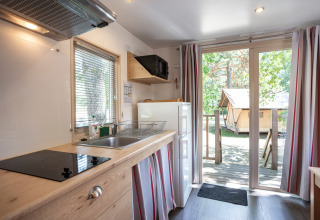 Cucina accogliente in cabina con porte a vetri e vista su veranda e tenda tra gli alberi all’esterno.