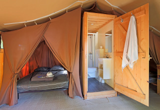 Interior de tienda safari con cama y baño en Tent Sweet de Huttopia Gorges du Tarn, Francia.