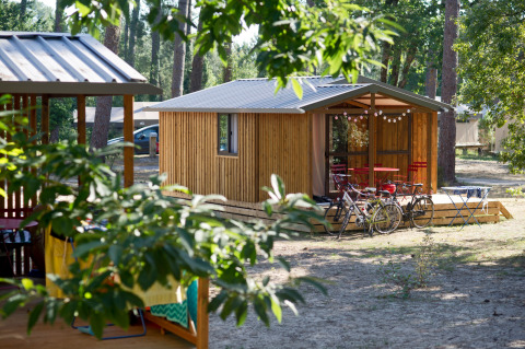 Udsigt til Chalet Evasion-hytte med cykler og siddeplads udenfor i Huttopia Landes Sud, Frankrig.