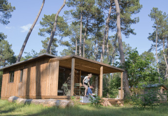 Cabaña de madera Chalet Ottawa en el bosque en Huttopia Landes Sud, Francia, con pareja en la terraza.