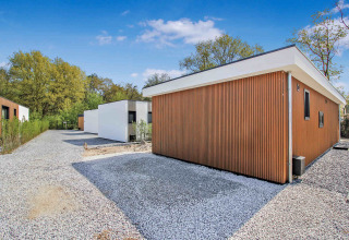 Moderne ferieboliger ved Uniq Leisure feriepark i Gelderland, Holland, omgivet af træer og grusstier.