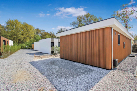 Moderne ferieboliger ved Uniq Leisure feriepark i Gelderland, Holland, omgivet af træer og grusstier.