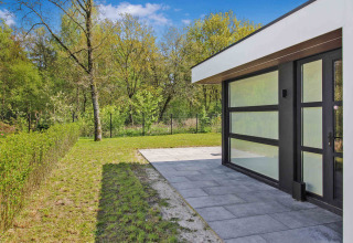 Moderne hytte med glasfacade og flisebelagt terrasse i Uniq Leisure feriepark, Gelderland, Holland.