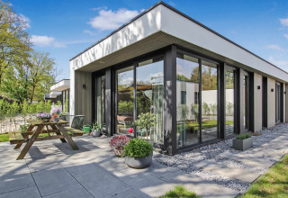 Moderne feriebolig med store vinduer, terrasse og grønne planter i Uniq Leisure feriepark, Gelderland, Holland.