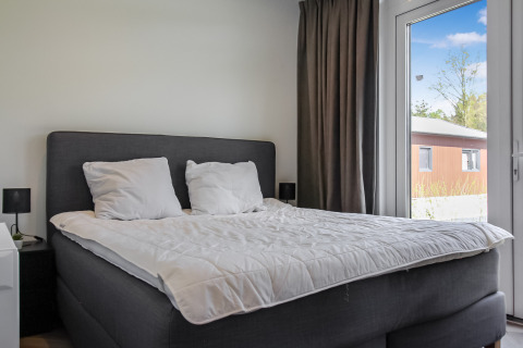 Dormitorio moderno con cama doble y grandes ventanas en Uniq Leisure, parque vacacional en Gelderland, Países Bajos.