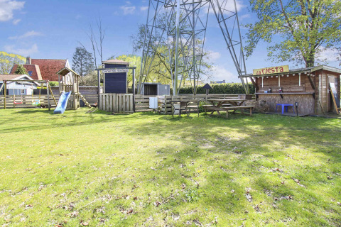 Playground with slide, picnic benches, and wooden huts at Uniq Leisure holiday park in Gelderland, Netherlands.