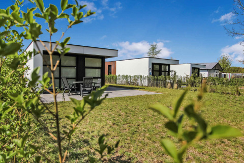 Modernas casas de vacaciones en el parque Uniq Leisure en Gelderland, Países Bajos, con césped verde y cielo azul.