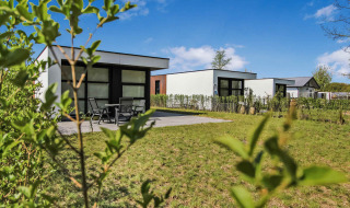 Modernas casas de vacaciones en el parque Uniq Leisure en Gelderland, Países Bajos, con césped verde y cielo azul.
