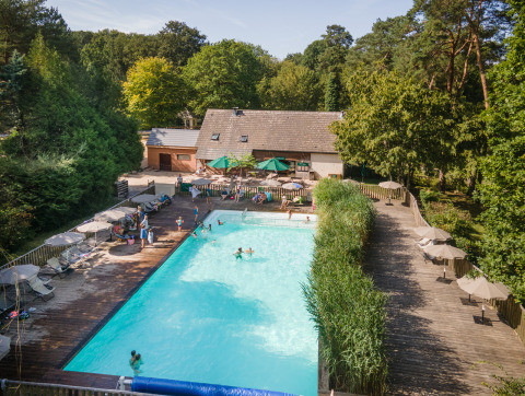 Piscina exterior rodeada de terraza de madera y tumbonas en Huttopia Rambouillet, parque vacacional en Île-de-France, Francia.