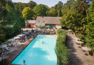 Piscina exterior rodeada de terraza de madera y tumbonas en Huttopia Rambouillet, parque vacacional en Île-de-France, Francia.