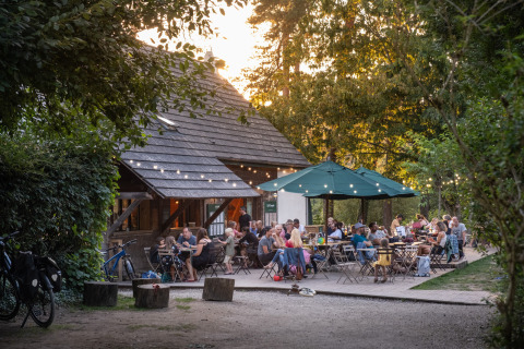 Personas cenando al aire libre bajo luces en Huttopia Rambouillet, parque vacacional en Île-de-France, Francia.