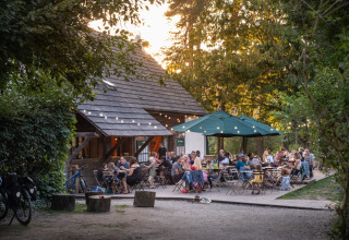 Folk nyder udendørs spisning under træerne ved en hyggelig café i Huttopia Rambouillet, Ile-de-France.