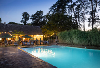 Piscina exterior iluminada al atardecer en el parque vacacional Huttopia Rambouillet, Île de France, Francia.
