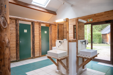 Baño interior de madera con lavabos y puertas verdes en Huttopia Rambouillet, Île de France, Francia.