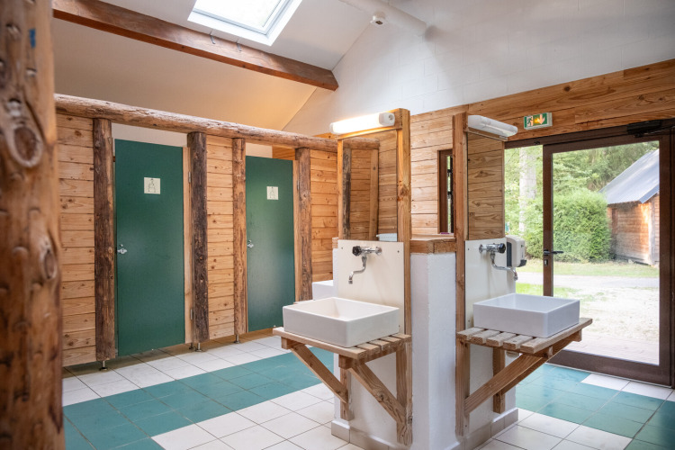 Wooden restroom with sinks and private stalls, natural light at Huttopia Rambouillet, Île de France, France.