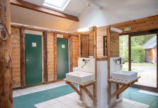 Wooden restroom with sinks and private stalls, natural light at Huttopia Rambouillet, Île de France, France.