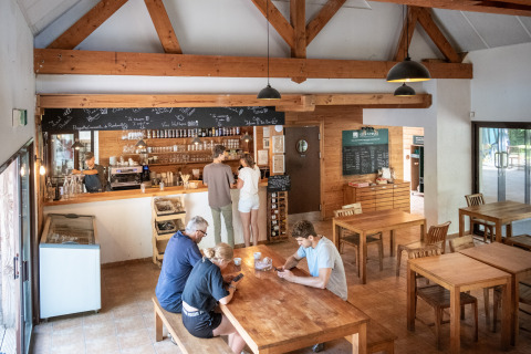 Interior luminoso de una cafetería en Huttopia Rambouillet con clientes sentados en mesas de madera.