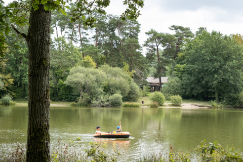 Twee personen varen in een opblaasboot op een meer bij Huttopia Rambouillet, omringd door bos in Île de France.