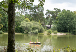 Zwei Personen paddeln in einem Schlauchboot auf einem See bei Huttopia Rambouillet im bewaldeten Île de France.