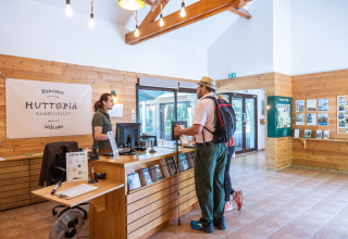 Mand med rygsæk taler med receptionist ved indtjekning på Huttopia Rambouillet feriepark i Frankrig.