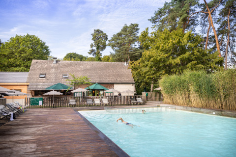 Piscina exterior en Huttopia Rambouillet, parque vacacional rodeado de árboles y tumbonas en Île de France, Francia.