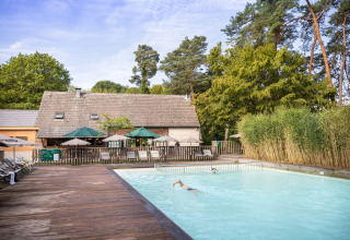 Udendørs swimmingpool ved Huttopia Rambouillet feriepark, omgivet af træer og liggestole i Île de France, Frankrig.
