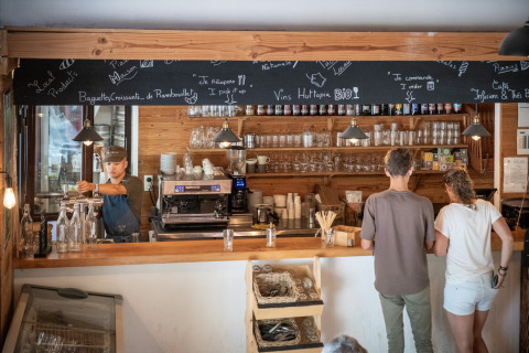 Mostrador de cafetería en Huttopia Rambouillet, parque vacacional de Île de France, con clientes y barista.