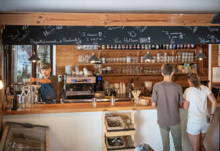 Caféområde i Huttopia Rambouillet, feriepark i Île de France, med gæster og medarbejder bag disken.