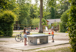 To børn spiller bordtennis udendørs i en feriepark med legeplads og volleyballbane på Huttopia Rambouillet.
