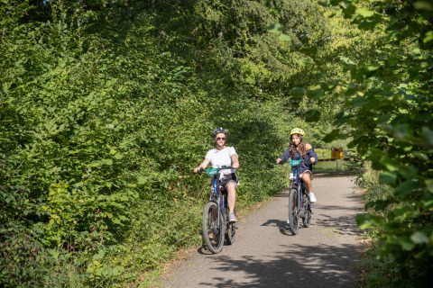 Deux personnes font du vélo sur un chemin verdoyant à Huttopia Rambouillet, Île de France, France.