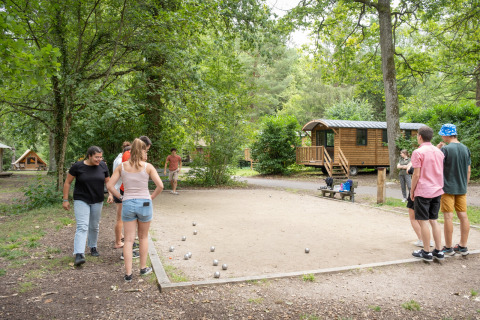 Personas juegan petanca junto a cabañas de madera en Huttopia Rambouillet, Île de France, Francia.