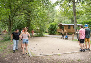 People play pétanque near wooden cabins surrounded by trees at Huttopia Rambouillet, Île de France, France.