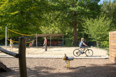 Children play volleyball and ride bikes in a sunny park area at Huttopia Rambouillet, Île de France, France.