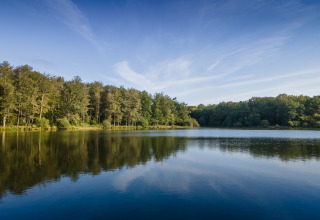 Rolig sø omgivet af træer under en klar blå himmel ved Huttopia Rambouillet feriepark, Île de France, Frankrig.