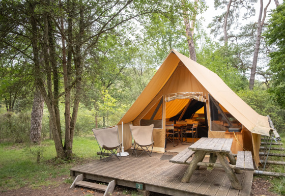 Tienda safari Canadienne con terraza de madera, dos sillas y una mesa de picnic en un bosque verde.